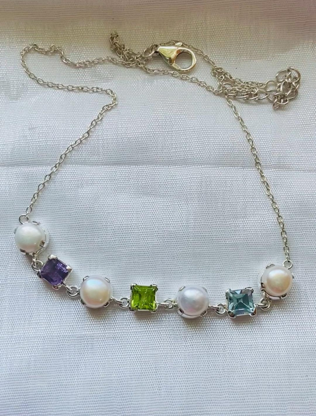 This necklace features a stunning blend of natural amethyst, peridot, and blue topaz stones set alongside lustrous freshwater pearls.
The gemstones are cushion-cut for a modern, elegant look, paired beautifully with round pearls for added charm.
Each stone is prong-set in 925 sterling silver, ensuring durability and a premium finish.
The alternating gemstone and pearl pattern creates a vibrant yet balanced aesthetic.
Designed for both casual and semi-formal wear, this piece adds color and grace to any outfi