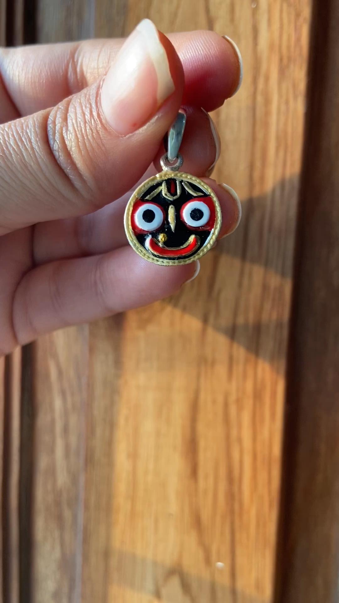 This Jagannath Pendant, handcrafted in 925 Sterling Silver, features the vibrant and iconic face of Lord Jagannath. The hand-painted enamel design in black, red, and white brings the deity to life, symbolizing divine blessings, positivity, and spiritual strength. Framed with a silver-plated gold-tone border, this religious pendant is a perfect blend of tradition and craftsmanship. Known as a protective talisman, it is ideal for those seeking good luck and sacred blessings.