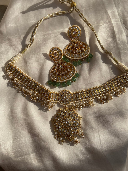 This Polki Necklace Set with Pearl and Emeralds is a luxurious example of traditional Indian jewelry, crafted in the sacred and timeless art of Kundan Meena and Meenakari work. Made in pure 925 sterling silver with a rich 22k gold plating, this handcrafted piece reflects the royal heritage of Jaipur, Rajasthan. The necklace features brilliant Polki stones and imitation emeralds, combined with delicate pearls that enhance its divine beauty